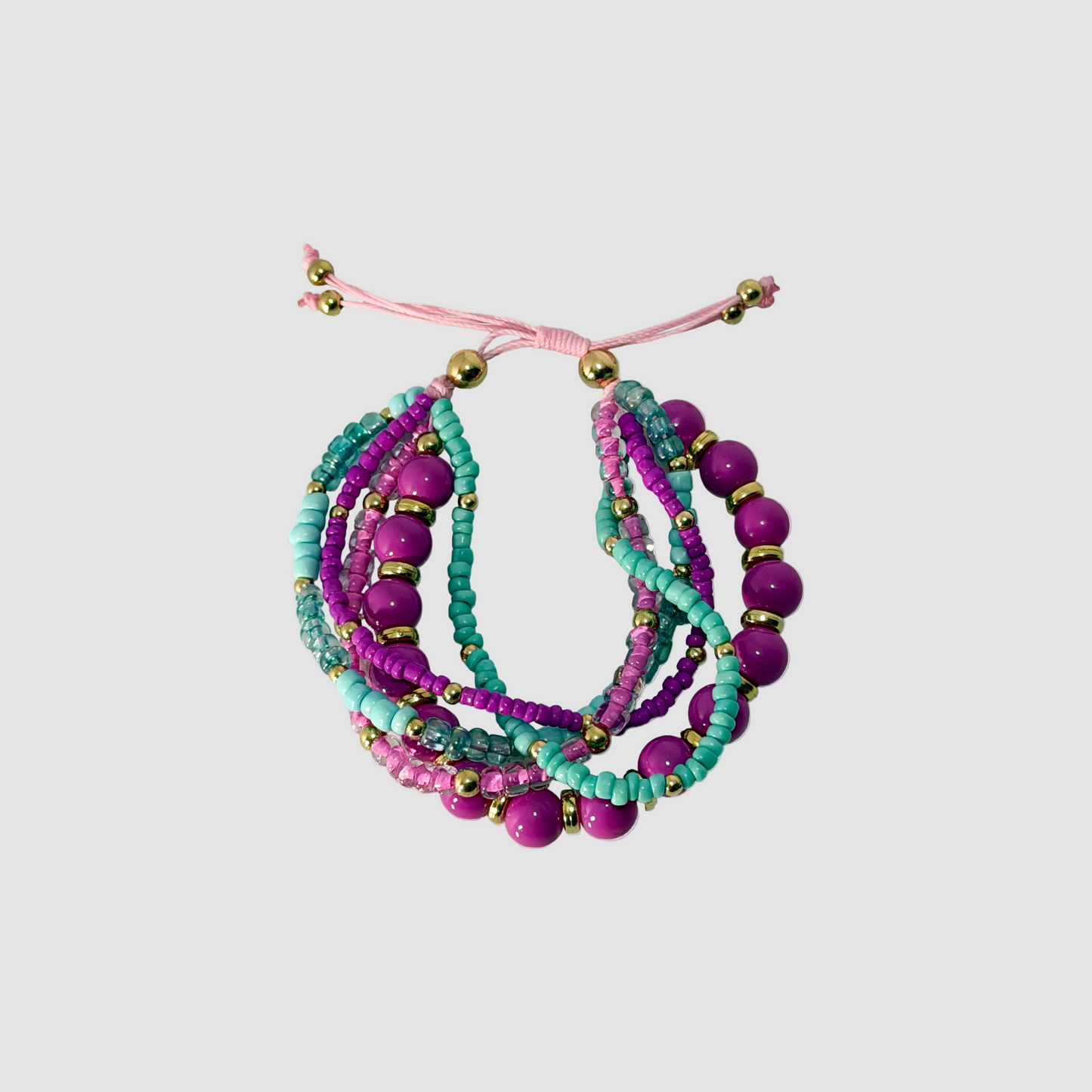 A multi-strand beaded wrap bracelet featuring vibrant purple, teal, and magenta beads with small gold spacer beads, tied with a pink adjustable cord on a solid gray background.