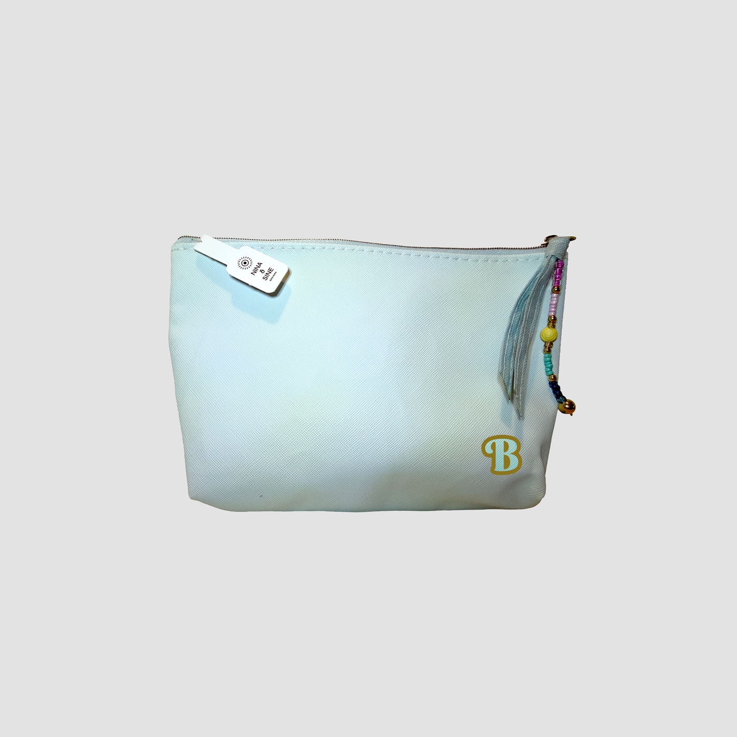 A light mint green zippered pouch with a gold 'B' initial on the bottom right, a white zipper pull tab, and a colorful beaded tassel charm, shown against a solid gray background.